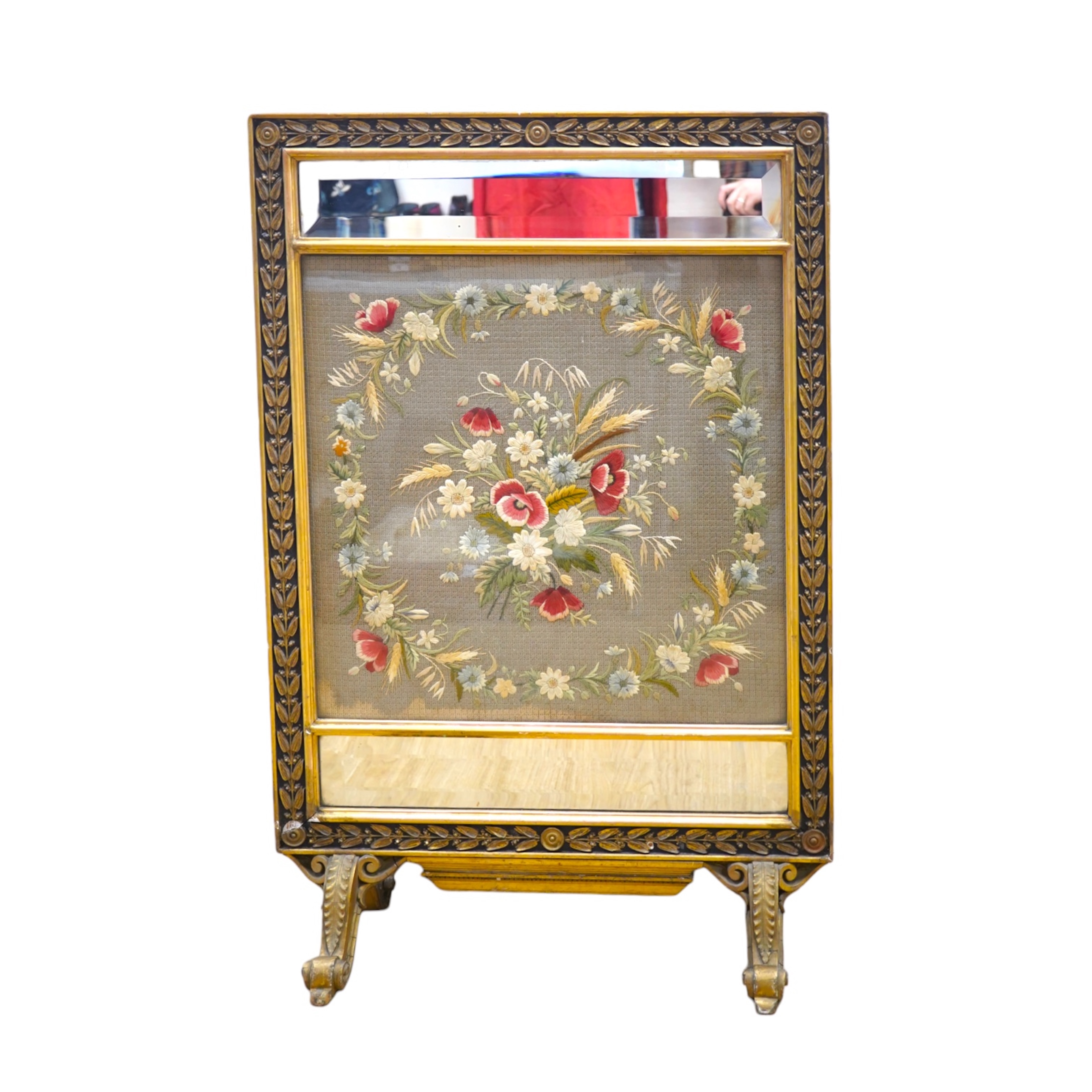 A late 19th century gilt framed silk and wool work embroidered fire screen, embroidered with a central sprig of poppies, wheat and wild flowers in a circular border of similar flowers, the frame with a decorative carved